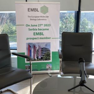 two chairs and a microphone on a table with an EMBL rollup banner with information on Serbia becoming an EMBL prospect member in the background