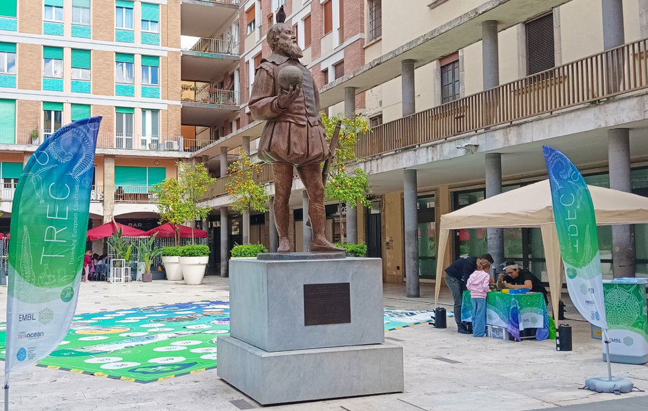 A public square in Italy, with a bronze statue of Galileo Galilei and a life size board game visible behind it.
