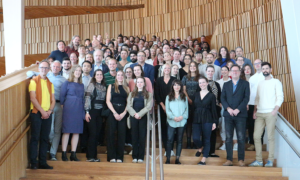 Group photo of the participants standing on wooden stairs with a wooden wall behind them.