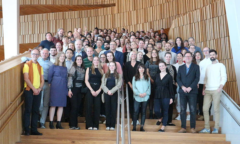 Group photo of the participants standing on wooden stairs with a wooden wall behind them.