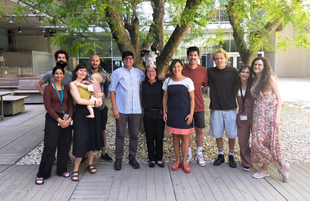 Group photo of 12 people in the inner courtyard of a building. Behind them there are two big trees with green leaves.