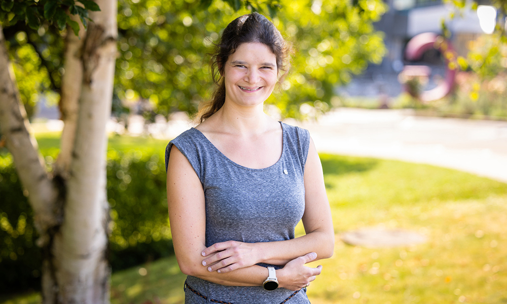 Woman with crossed arms stands in front of tree