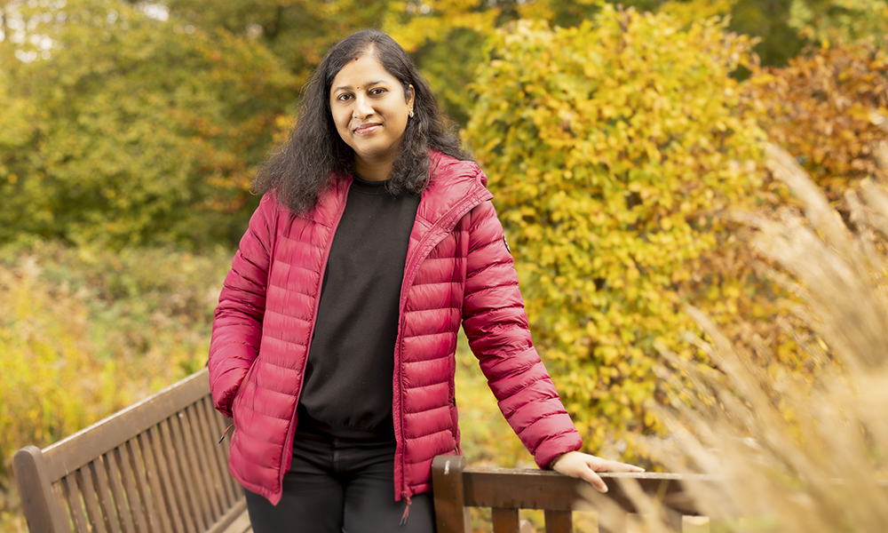 Woman in red jacket outdoors with fall foliage behind her