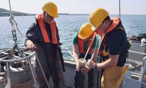 Three men working on a boat, with the ocean in the background