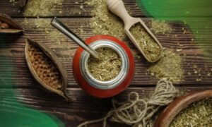 A cup of yerba mate on a wooden surface and some dried yerba mate next to it.