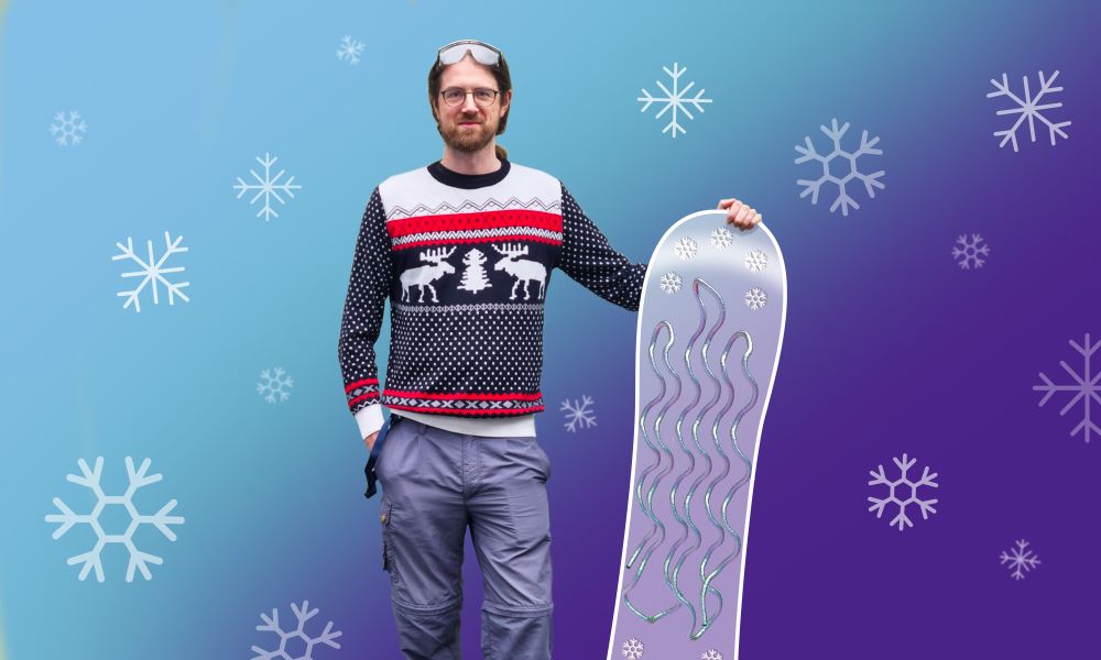 Photo of Yehudi wearing a Christmas jumper and lab goggles, standing next to snowboard. The snowboard features an overlaid illustration of the snow flea antifreeze protein structure, which resembles a flat sheet made of a folded wavy string.