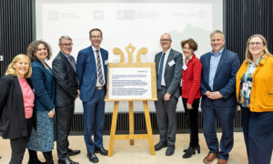 Eight people standing next to plaque on an easel.